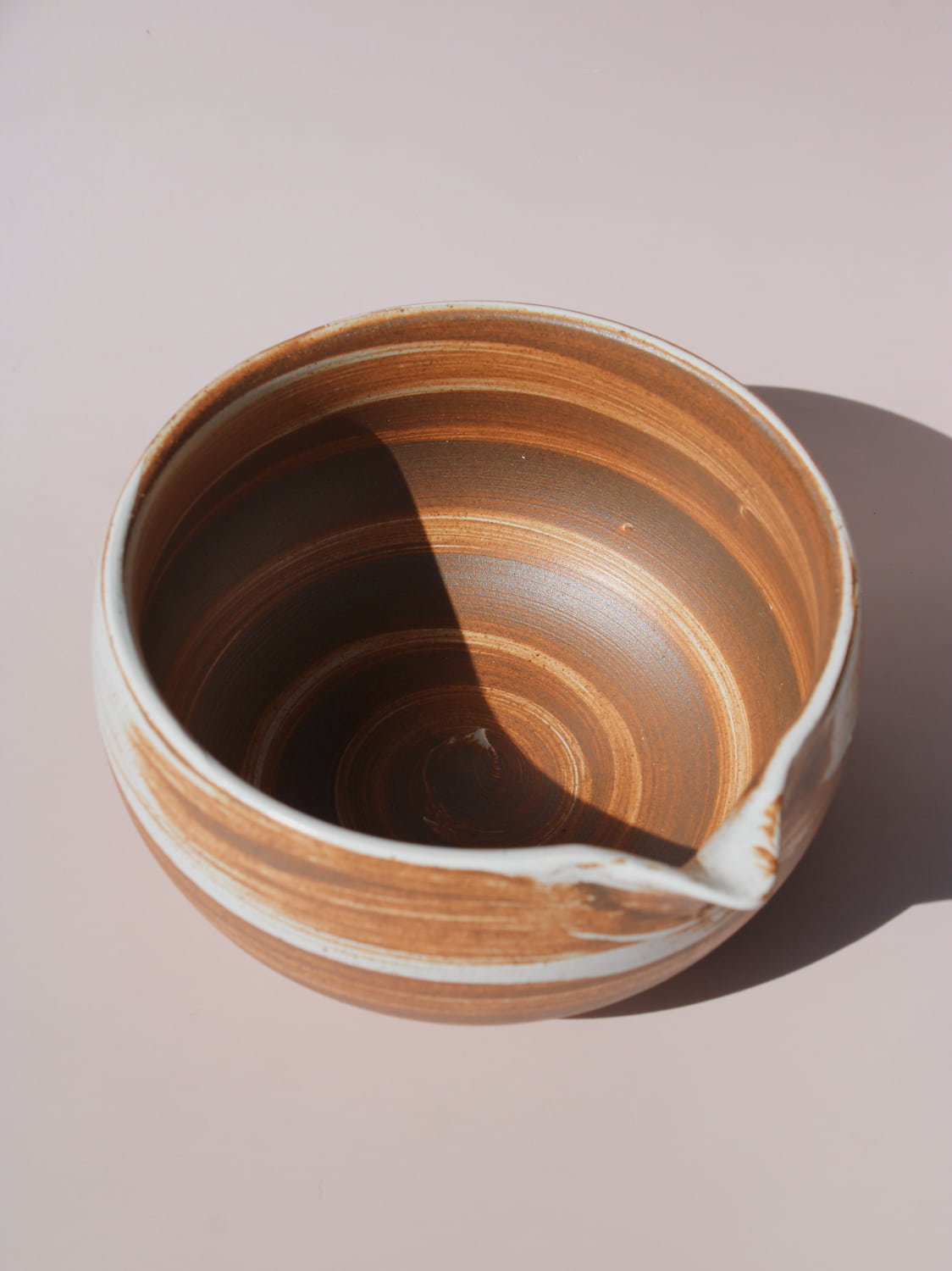 Kanso Matcha Bowl in warm terracotta with white swirl glaze detail and a pouring spout, on a soft pink background.