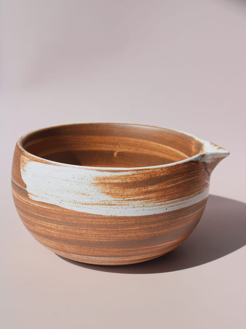 Kanso Matcha Bowl in warm terracotta with white swirl glaze detail and a pouring spout, on a soft pink background.