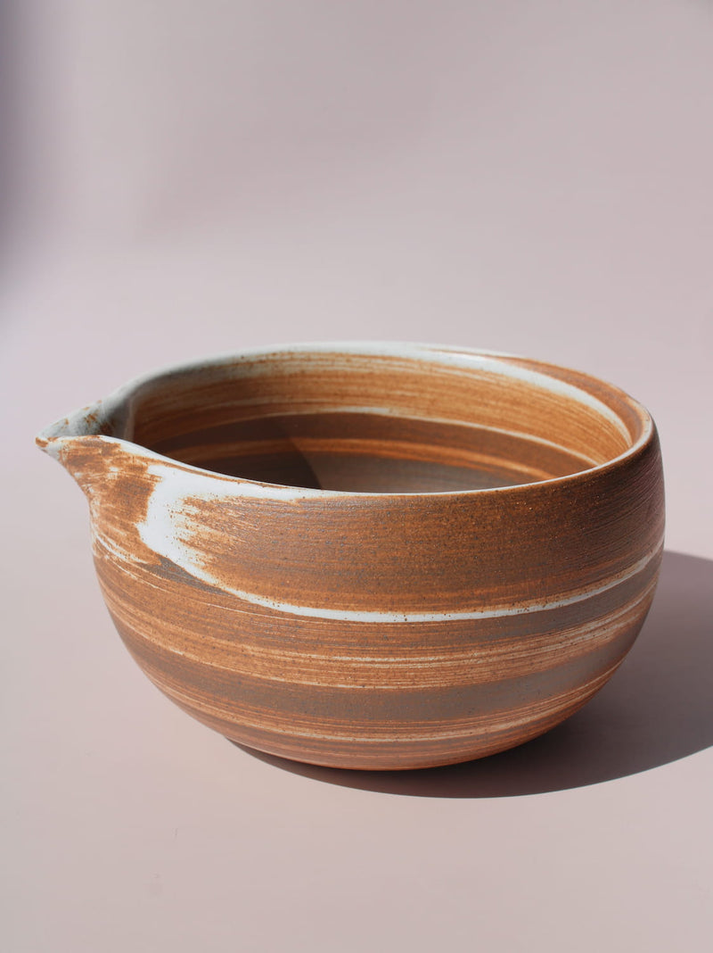 Kanso Matcha Bowl in warm terracotta with white swirl glaze detail and a pouring spout, on a soft pink background.