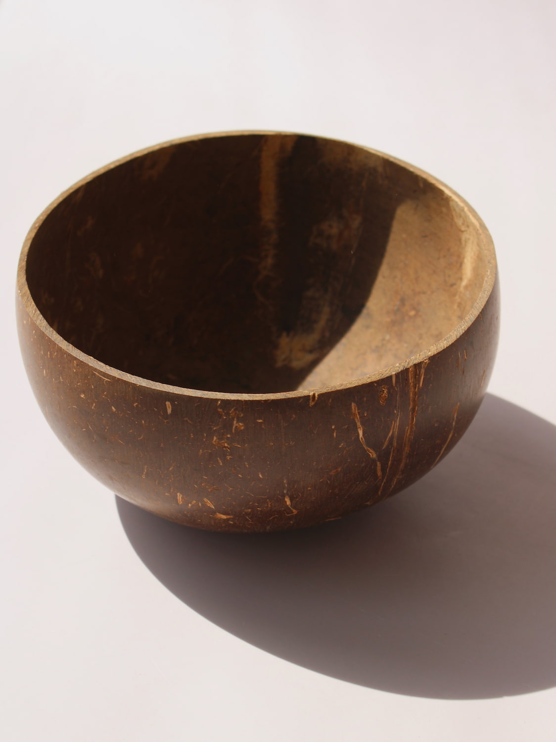 Nari Coconut Bowl in natural dark brown coconut shell with organic texture and smooth interior, on a soft pink background.