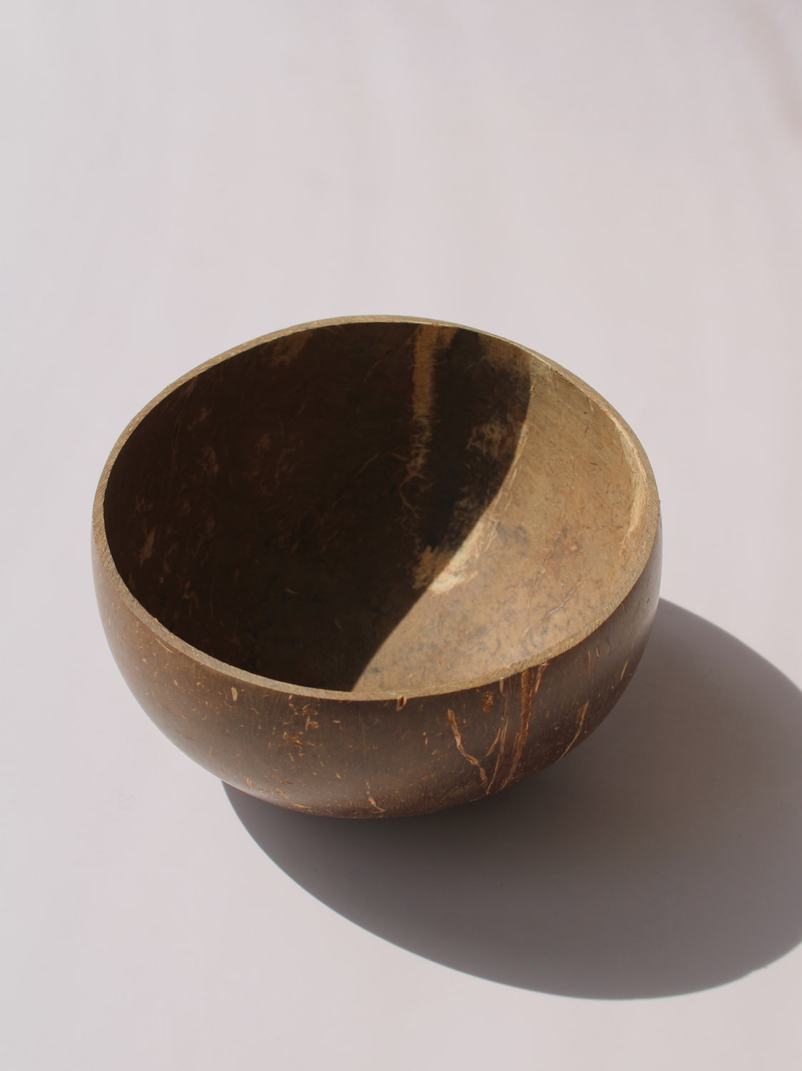 Nari Coconut Bowl in natural dark brown coconut shell with organic texture and smooth interior, on a soft pink background.