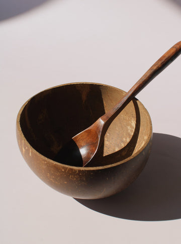 Nari Coconut Bowl in natural dark brown coconut shell with organic texture and smooth interior, on a soft pink background.