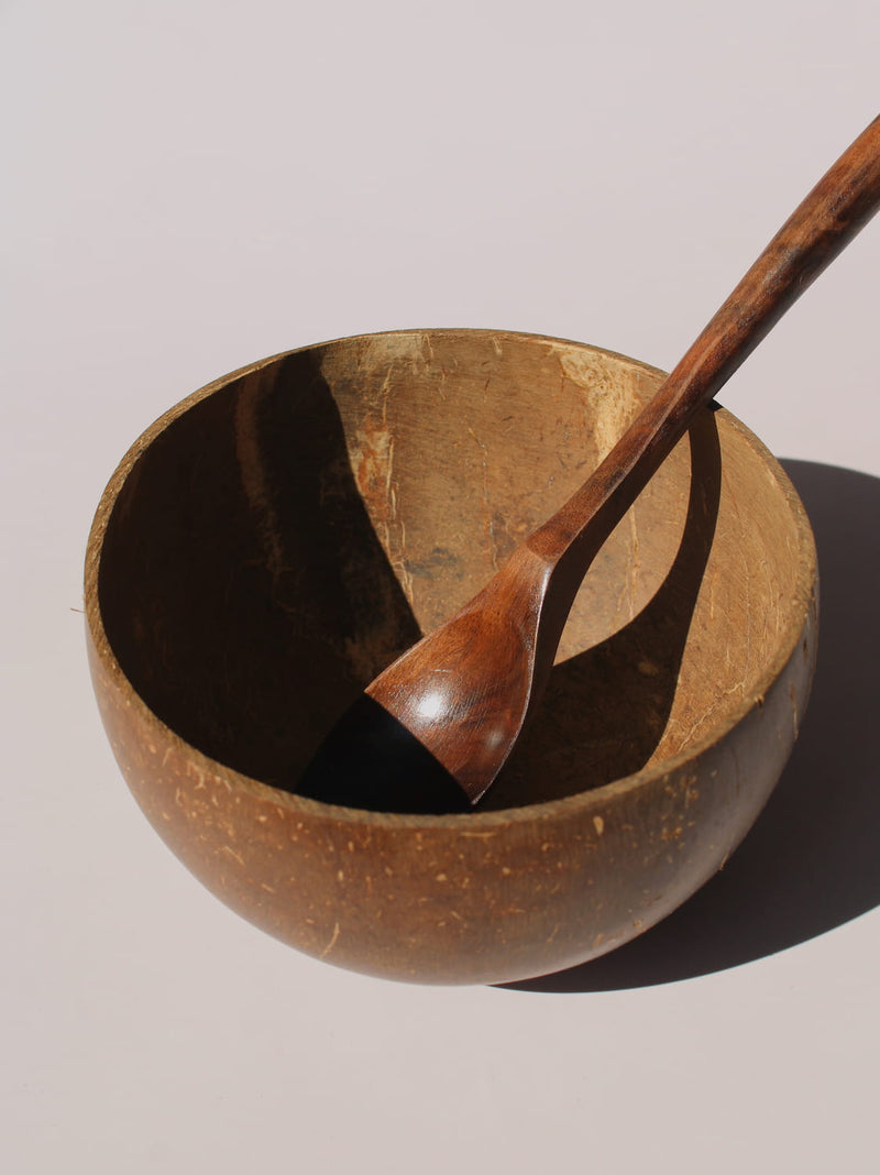 Nari Coconut Bowl in natural dark brown coconut shell with organic texture and smooth interior, on a soft pink background.