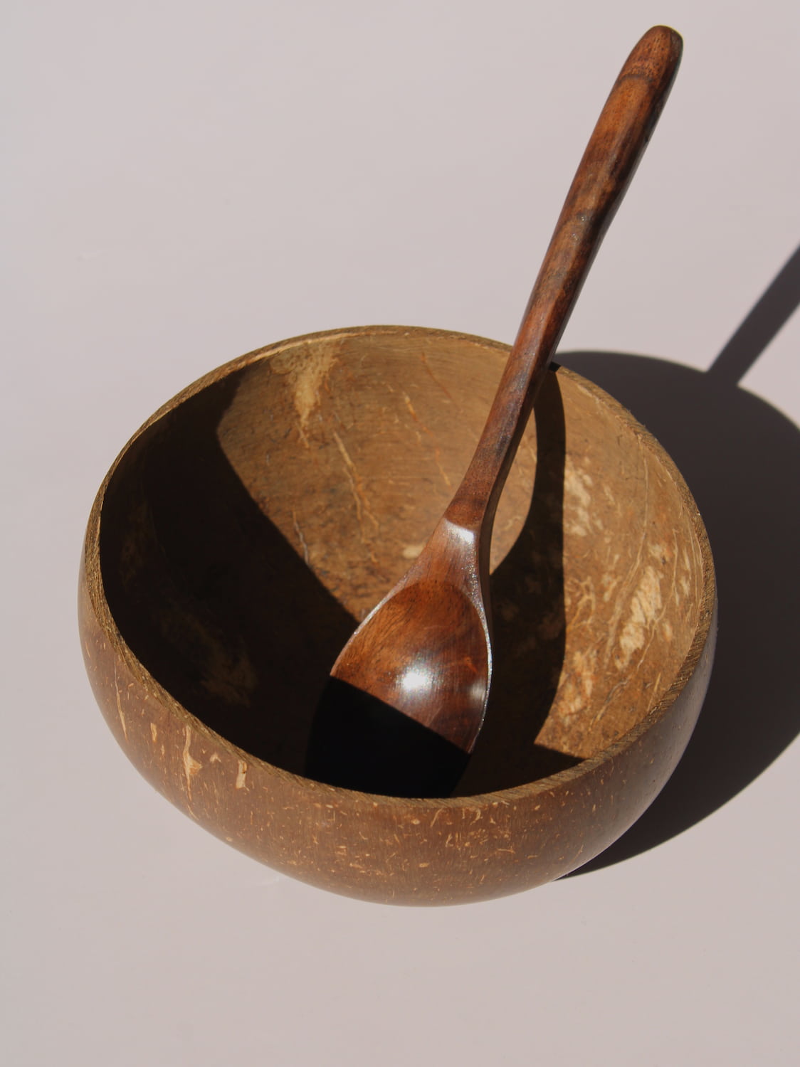 Nari Coconut Bowl in natural dark brown coconut shell with organic texture and smooth interior, on a soft pink background.