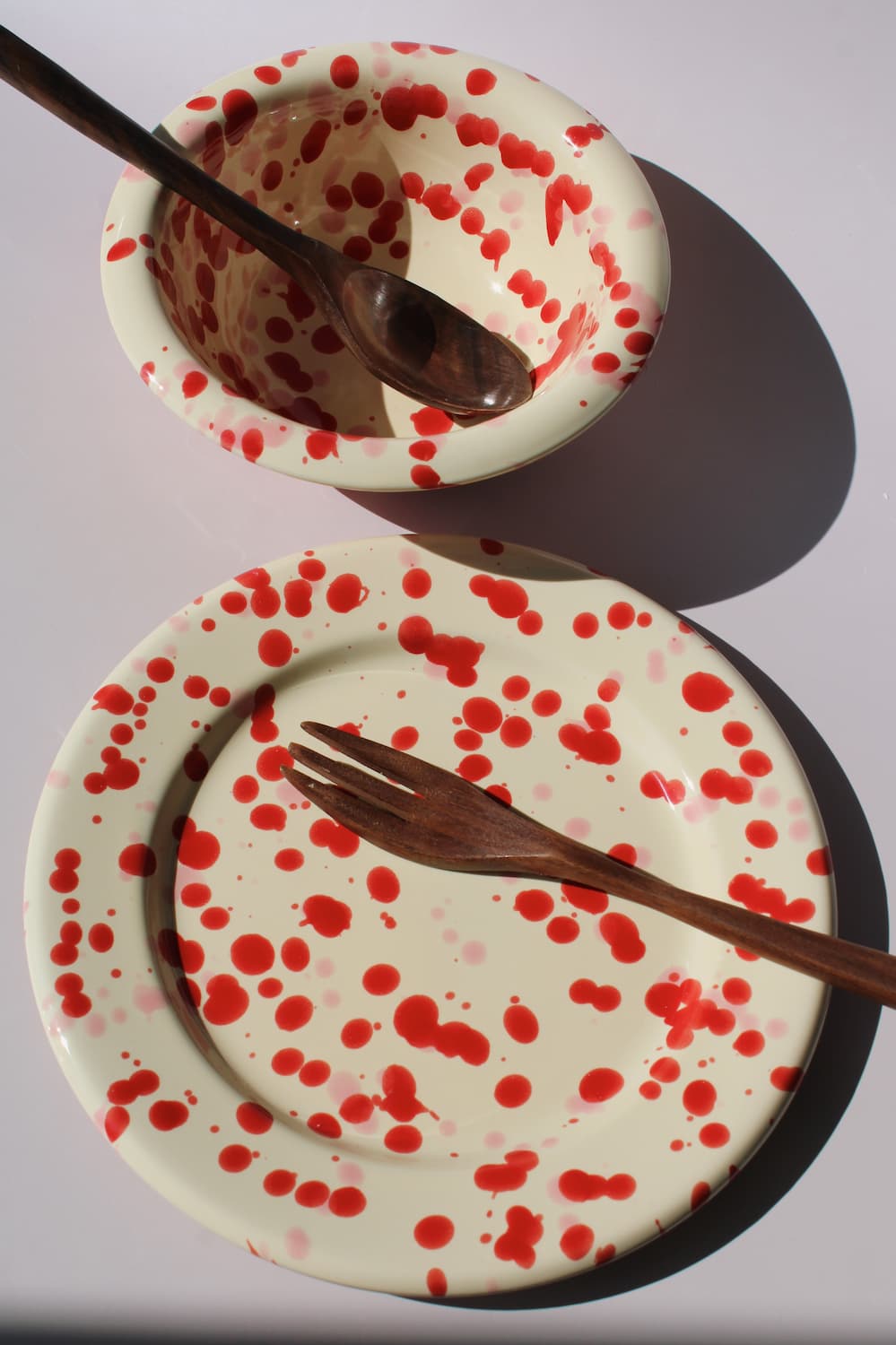 Dotty Ceramic Bowl and Dotty Ceramic Plate, a matching cream dinnerware set with red speckled dot pattern, on a soft pink background.