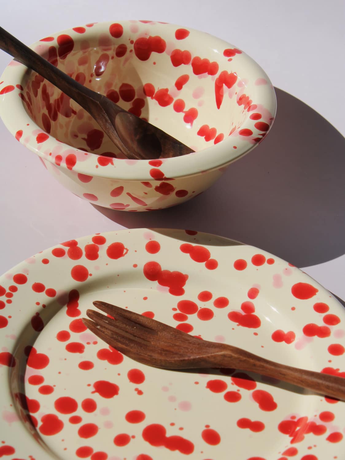 Dotty Ceramic Bowl and Dotty Ceramic Plate, a matching cream dinnerware set with red speckled dot pattern, on a soft pink background.