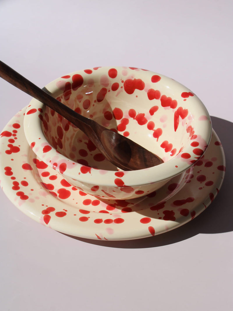 Dotty Ceramic Bowl and Dotty Ceramic Plate, a matching cream dinnerware set with red speckled dot pattern, on a soft pink background.