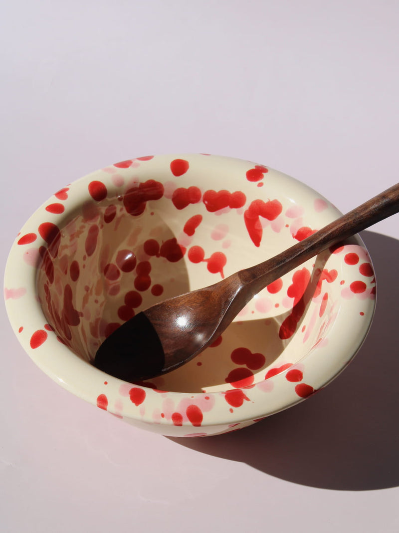 Dotty Ceramic Bowl in cream with red speckled dot pattern, paired with a wooden serving spoon, on a soft pink background.