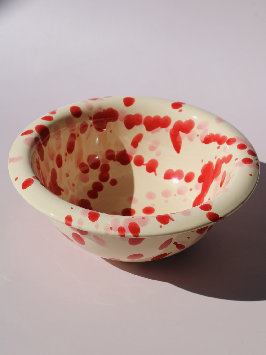 Dotty Ceramic Bowl in cream with red speckled dot pattern, paired with a wooden serving spoon, on a soft pink background.