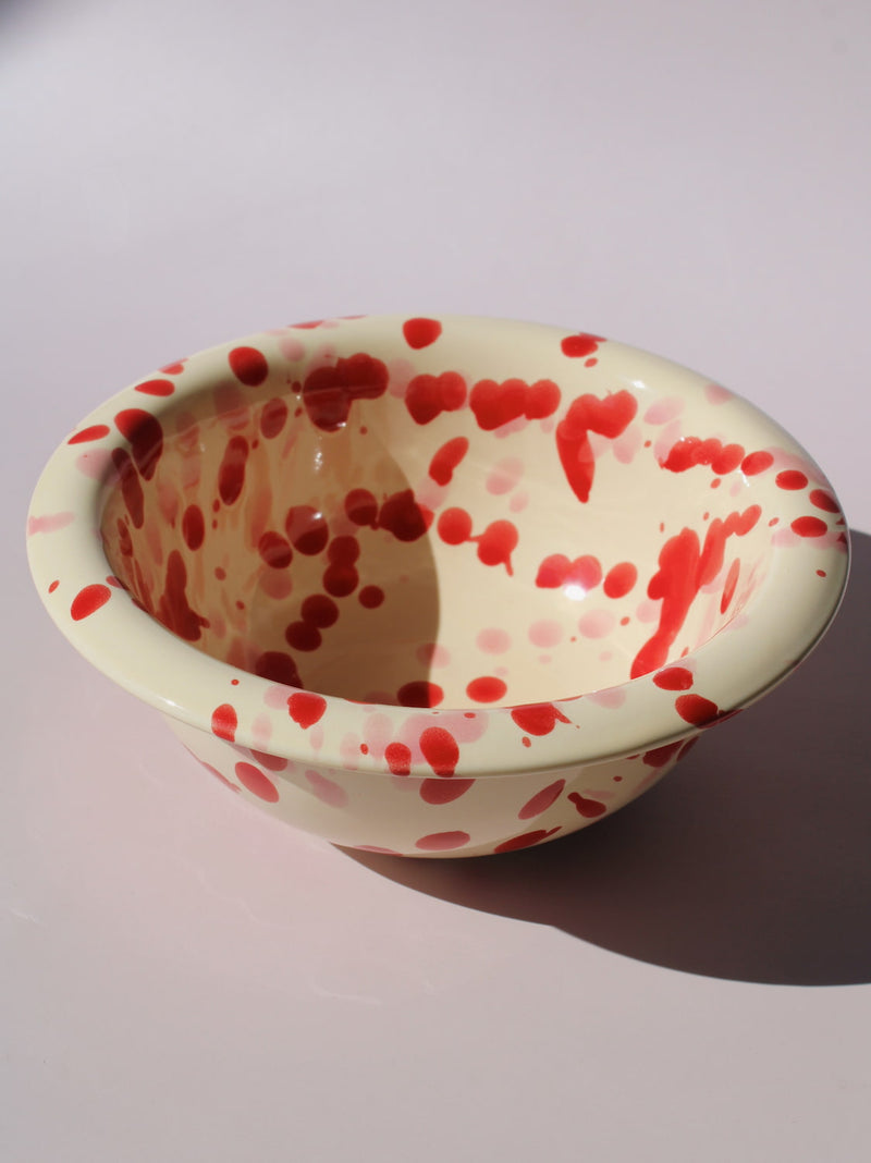 Dotty Ceramic Bowl in cream with red speckled dot pattern, paired with a wooden serving spoon, on a soft pink background.