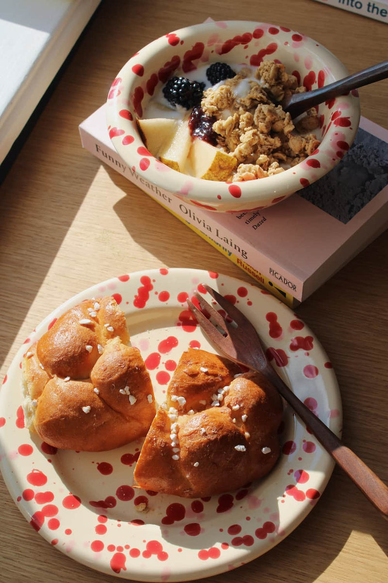 Dotty Ceramic Bowl and Dotty Ceramic Plate in matching cream with red speckled dot pattern, styled with a morning granola bowl and brioche.