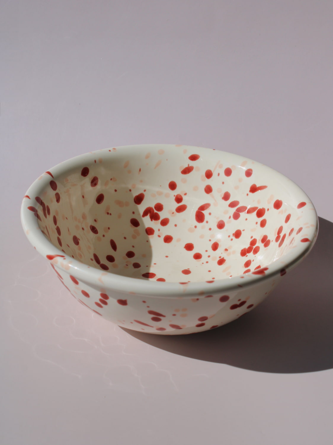 Bera Ceramic Bowl in cream with red speckled dot pattern, paired with a wooden serving spoon, on a soft pink background.
