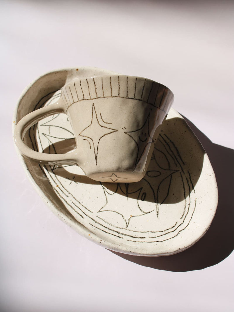 Mythos Ceramic Plate and Astral Ceramic Mug in matching speckled cream with hand-etched star and botanical line drawings, styled together on a soft white background.