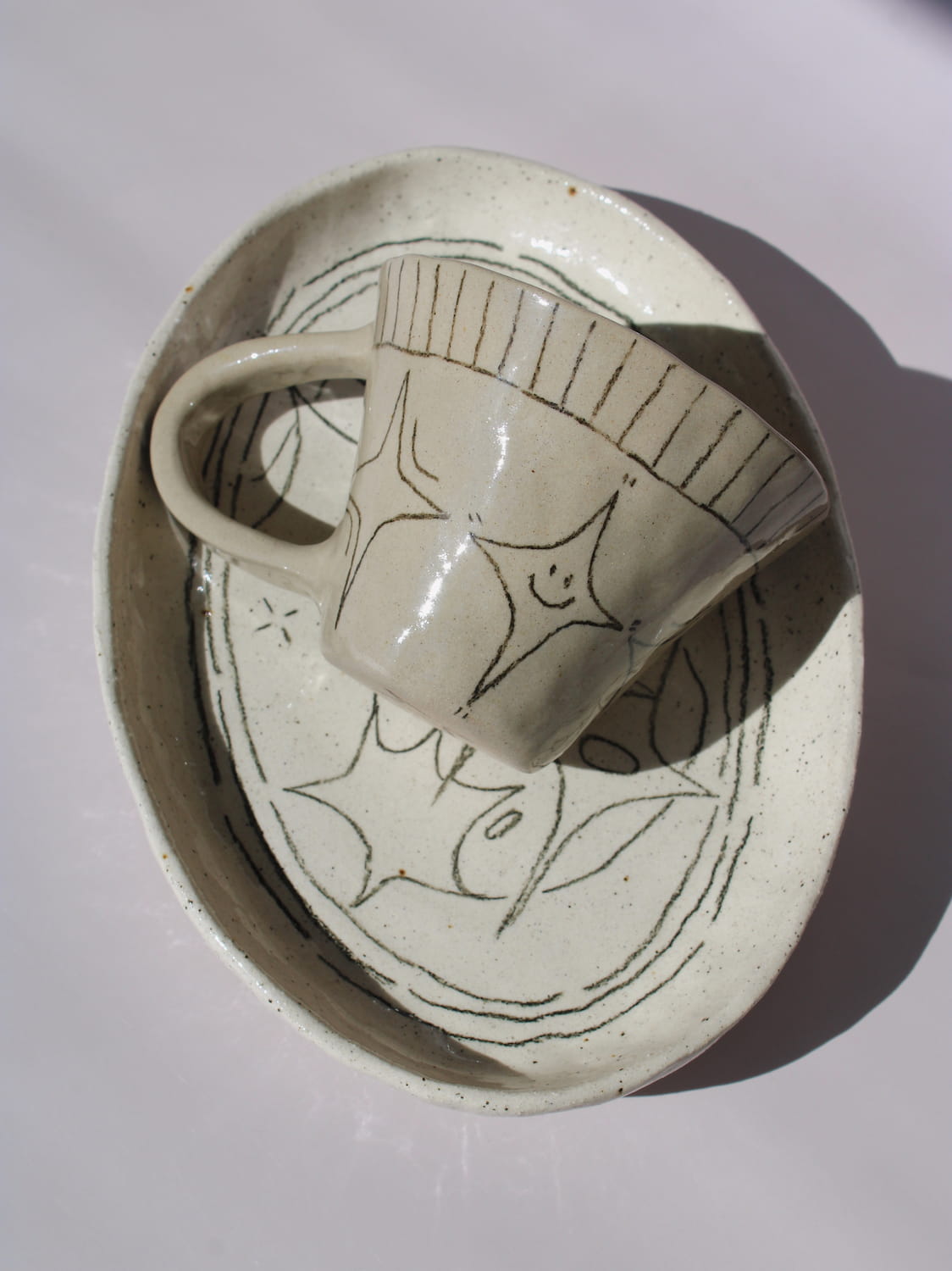 Mythos Ceramic Plate and Astral Ceramic Mug in matching speckled cream with hand-etched star and botanical line drawings, styled together on a soft white background.