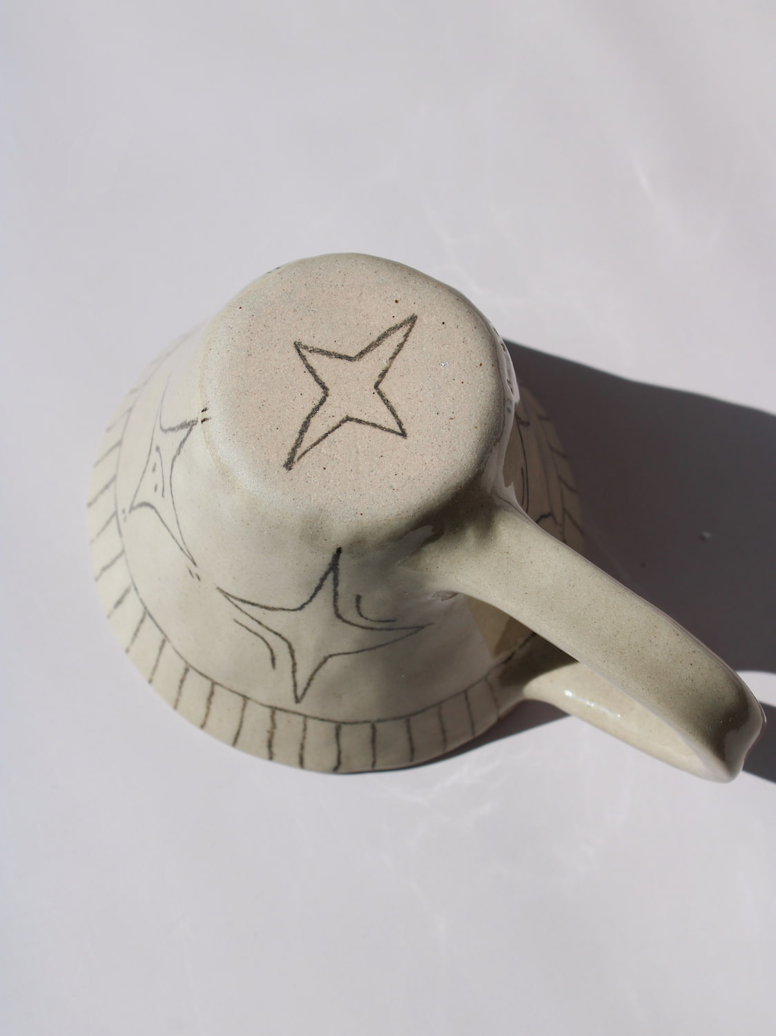 Astral Ceramic Mug in speckled cream with hand-etched four-point star and smiley face motifs and a stripe rim detail, on a soft white background.