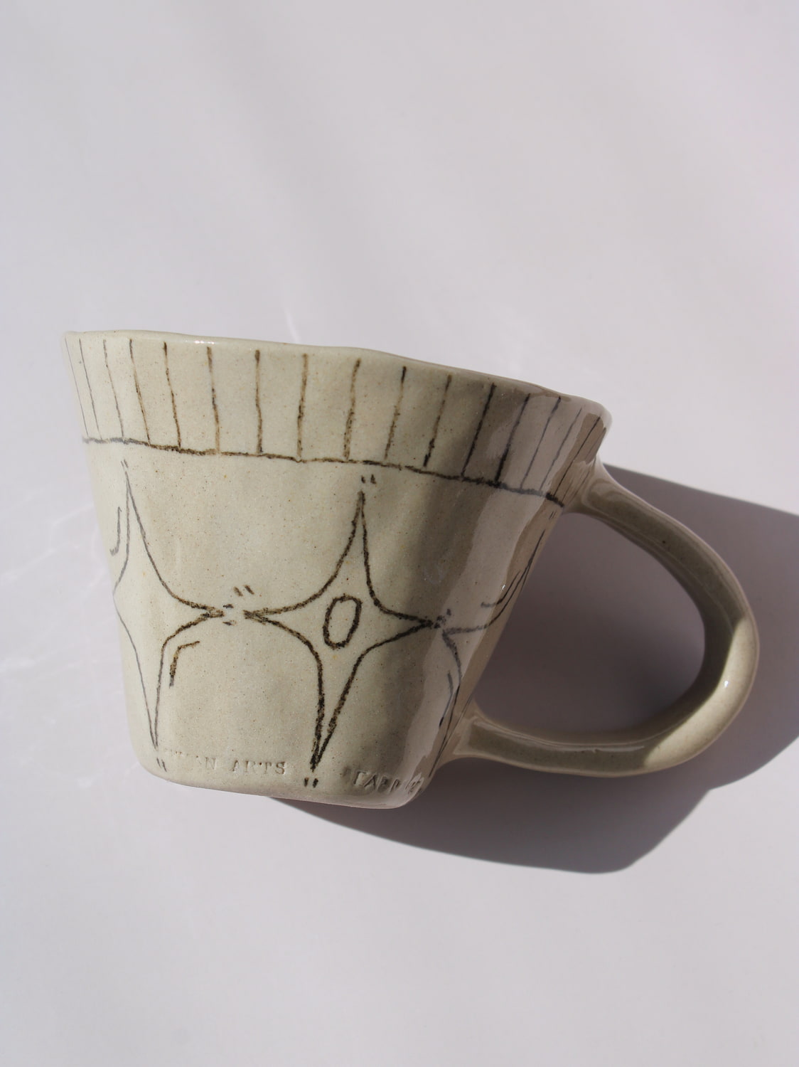 Astral Ceramic Mug in speckled cream with hand-etched four-point star and smiley face motifs and a stripe rim detail, on a soft white background.