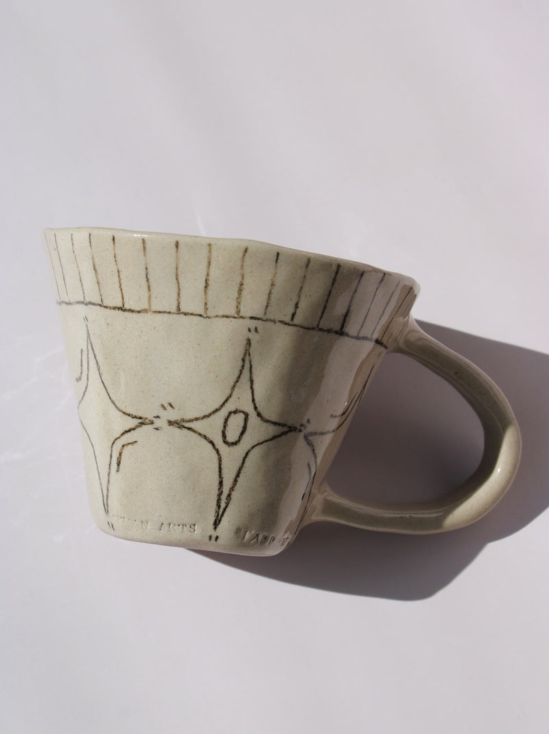 Astral Ceramic Mug in speckled cream with hand-etched four-point star and smiley face motifs and a stripe rim detail, on a soft white background.