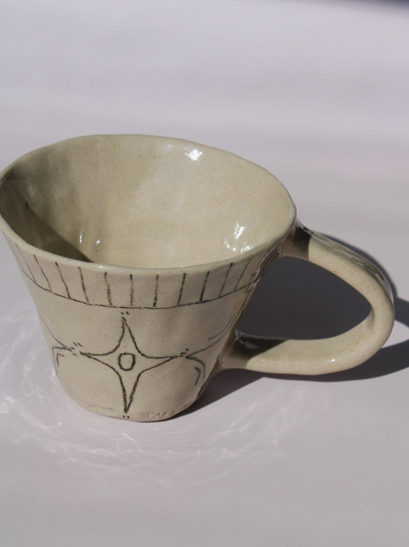 Astral Ceramic Mug in speckled cream with hand-etched four-point star and smiley face motifs and a stripe rim detail, on a soft white background.
