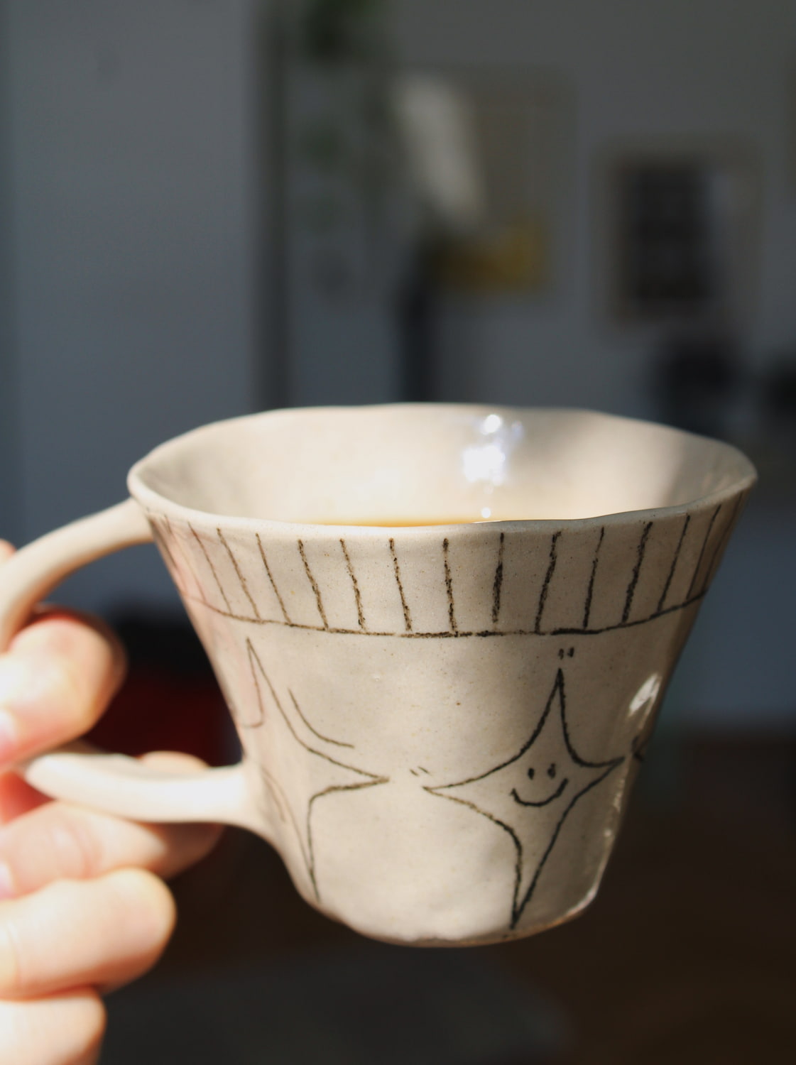 Astral Ceramic Mug in speckled cream with hand-etched star and stripe detail, held in hand filled with a latte, with a blurred indoor background in natural light.