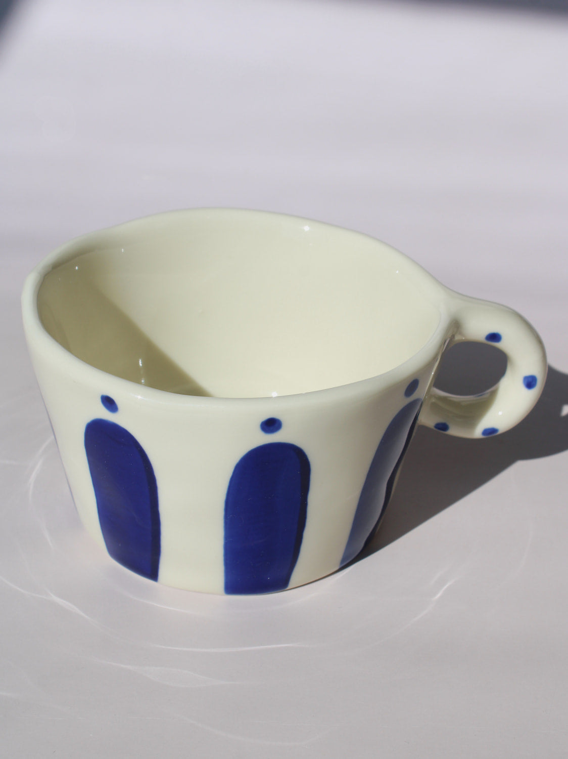 Enzo Ceramic Mug with bold blue arch stripes and polka dot handle on cream base, handmade pottery coffee mug