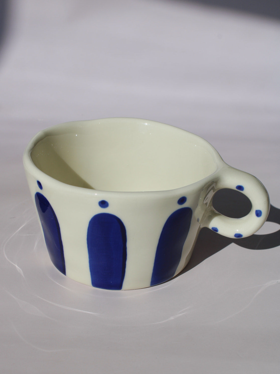 Enzo Ceramic Mug with bold blue arch stripes and polka dot handle on cream base, handmade pottery coffee mug