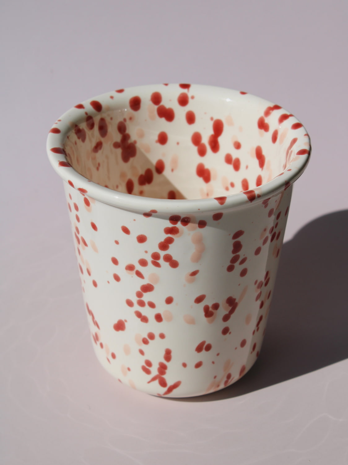 Bera Ceramic Cup in cream with red speckled dot pattern, on a soft pink background.