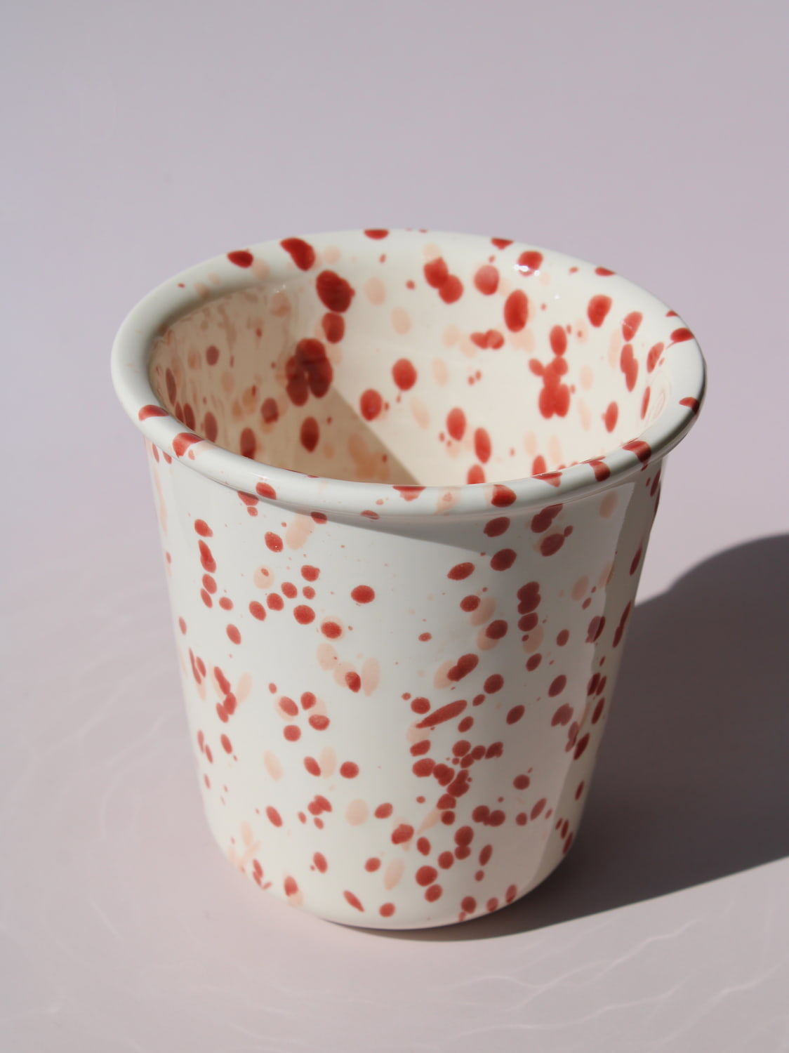 Bera Ceramic Cup in cream with red speckled dot pattern, on a soft pink background.
