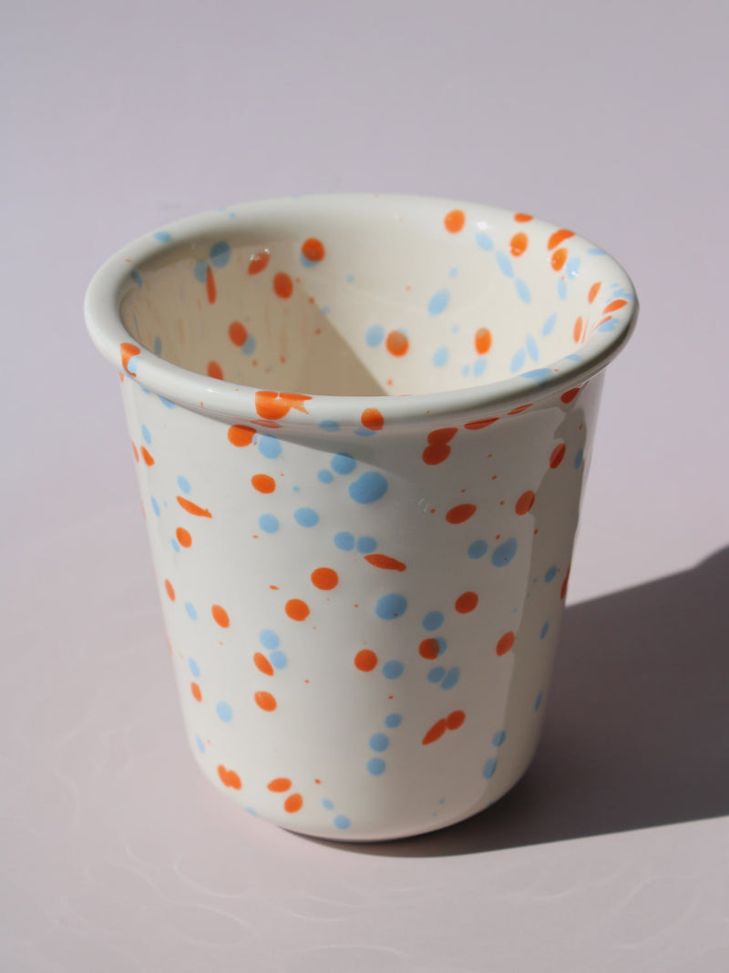 Naro Ceramic Cup in cream with orange and blue speckled dot pattern, on a soft pink background.