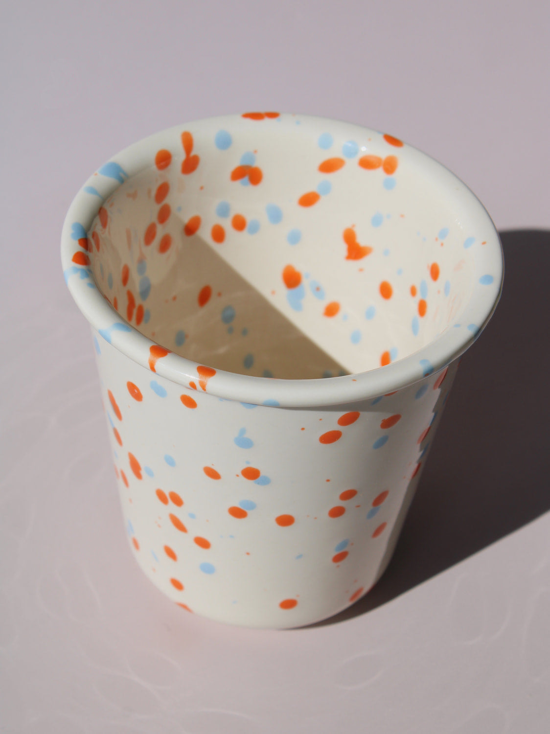 Naro Ceramic Cup in cream with orange and blue speckled dot pattern, on a soft pink background.