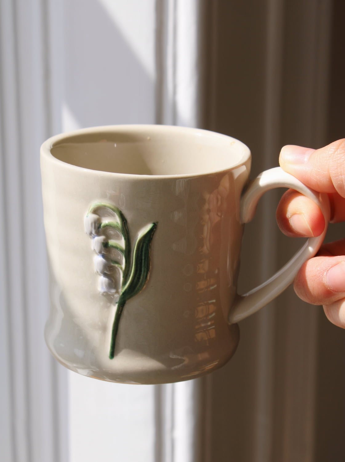 Bellis ceramic mug with delicate leaf motif held in hand by window in soft natural light
