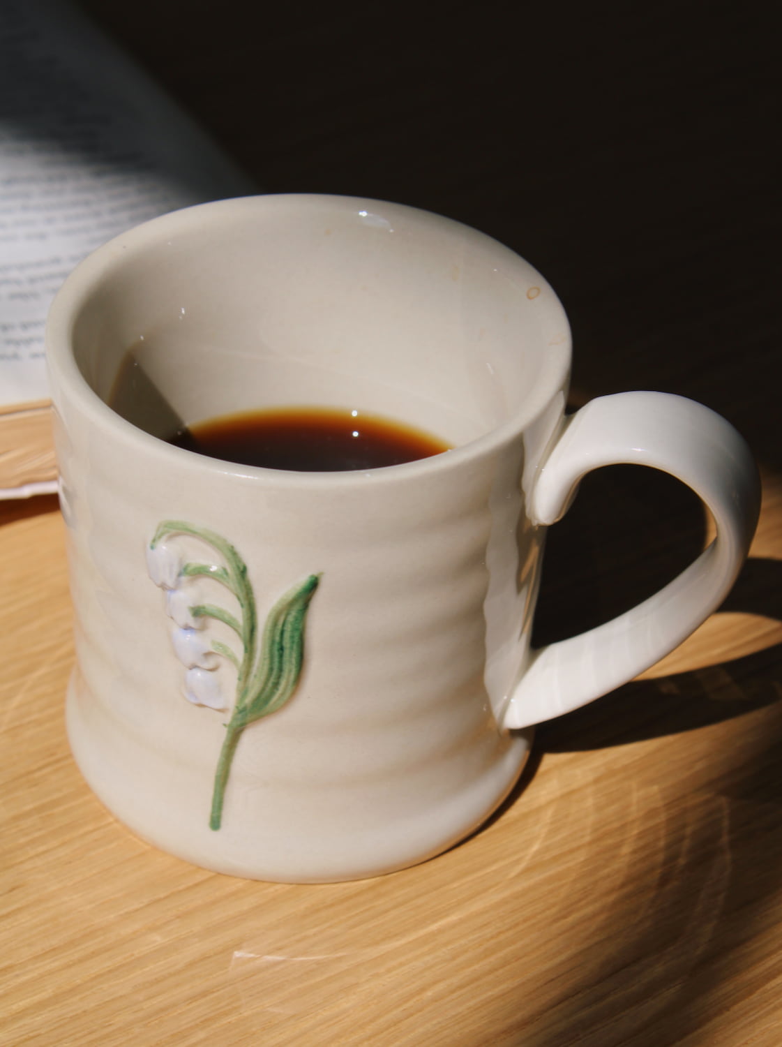 Handmade Bellis ceramic mug with green botanical detail on wooden table.