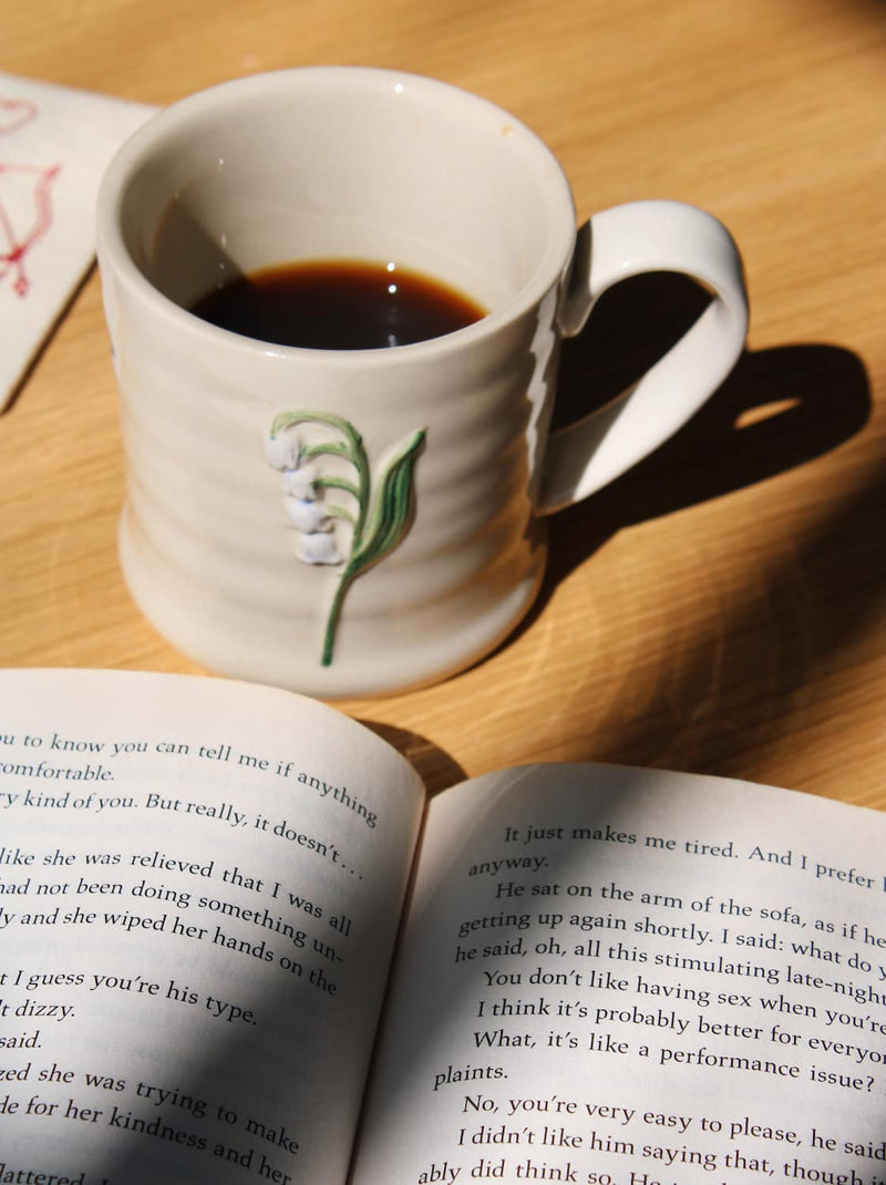 Bellis ceramic mug filled with coffee styled on open book in warm sunlight.