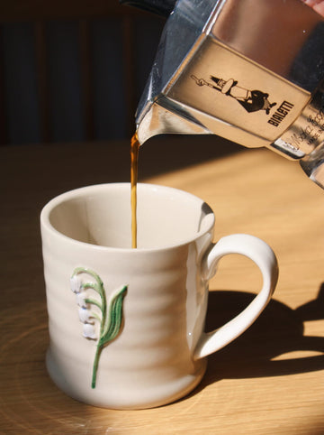 Bellis ceramic mug with coffee being poured, minimal cozy morning setting.