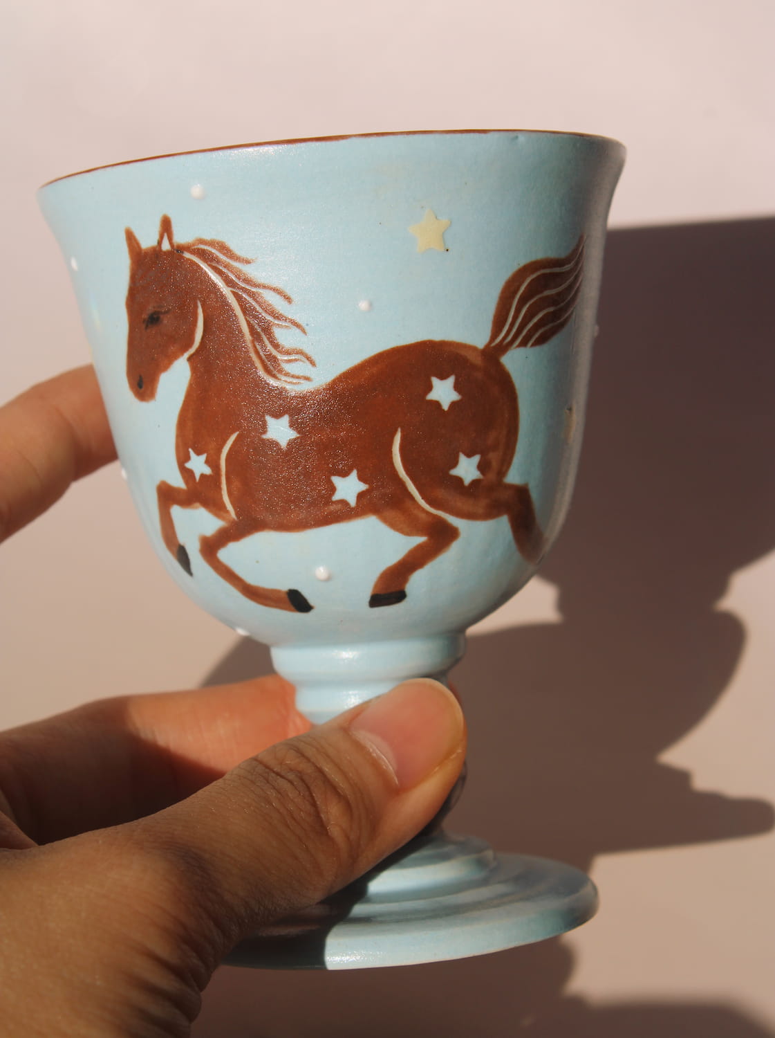 Hand-painted ceramic goblet with running horse motif and star details on light blue glaze.