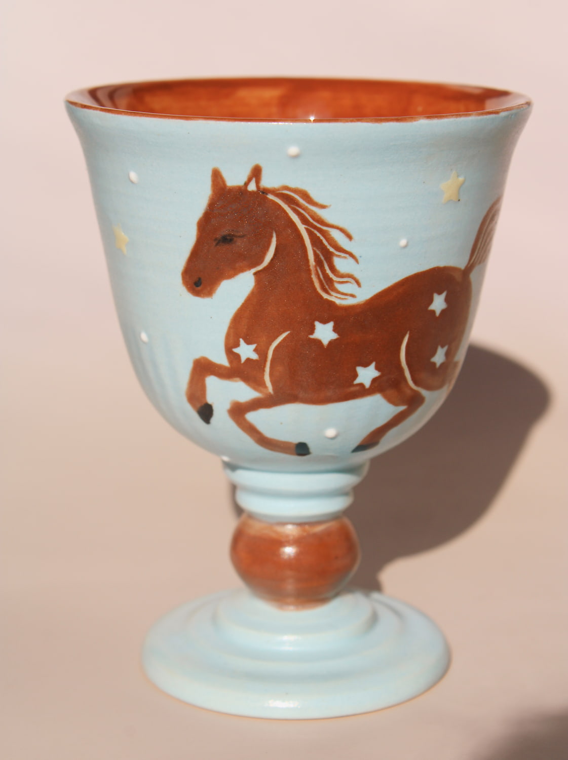 Hand-painted ceramic goblet with running horse motif and star details on light blue glaze.