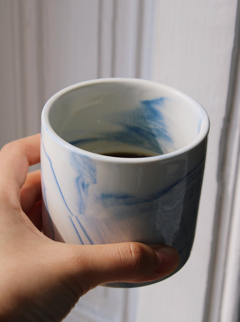 Handmade Sumi ceramic cup held in hand with minimalist blue glaze detail.