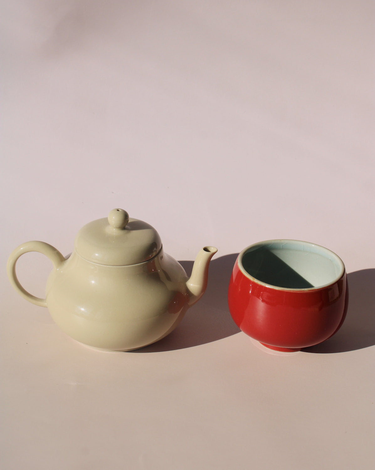Sumi ceramic tea set with soft sage teapot pouring into a round red tea cup, minimalist handmade tea set for modern tea rituals.