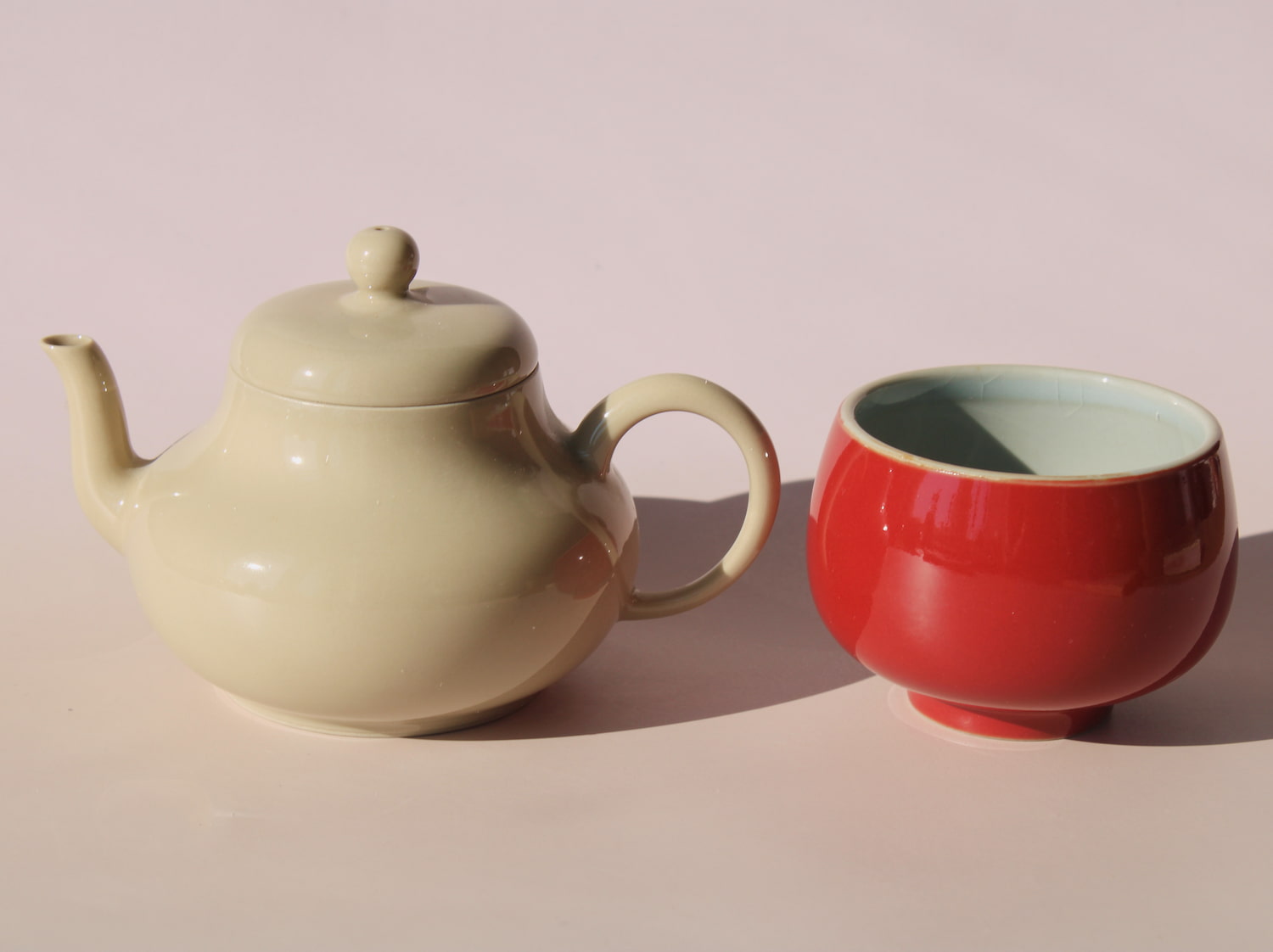Sumi ceramic tea set with soft sage teapot pouring into a round red tea cup, minimalist handmade tea set for modern tea rituals.