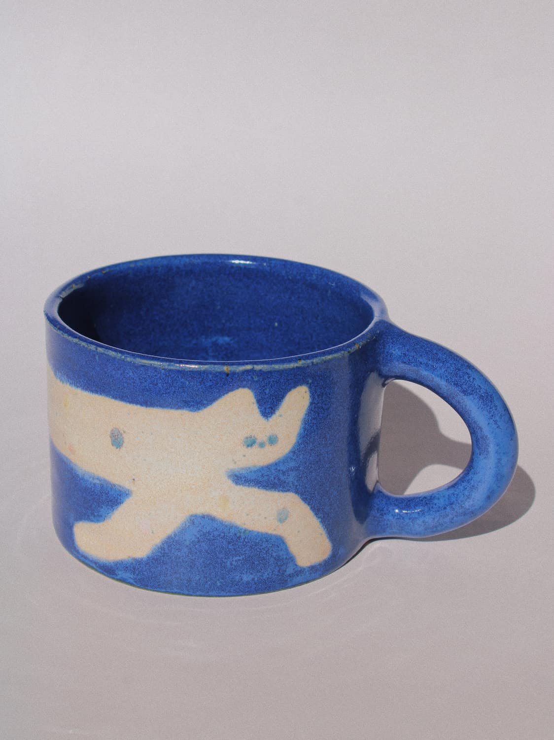 Moonmilk Cat Ceramic Mug by Marta Shurpakova – handmade blue ceramic mug with a playful cat design on a pink background