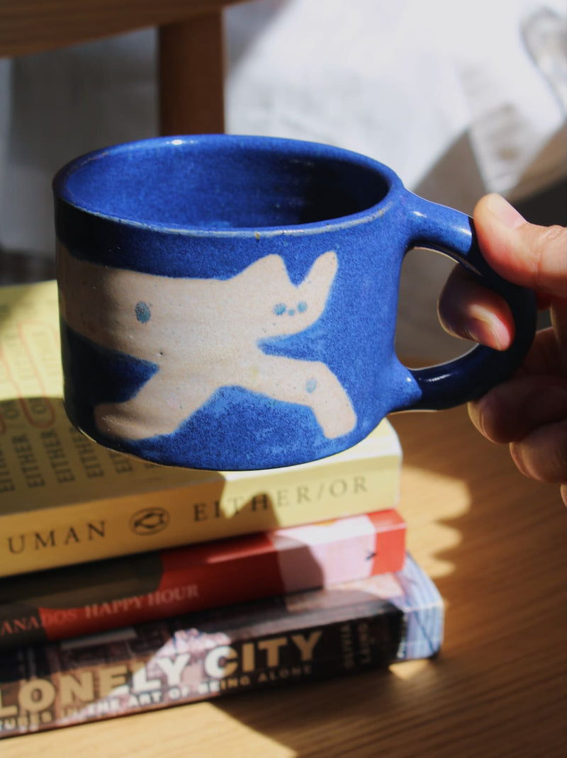 Moonmilk Cat Ceramic Mug by Marta Shurpakova – handmade blue ceramic mug with a playful cat design in a cosy home setting