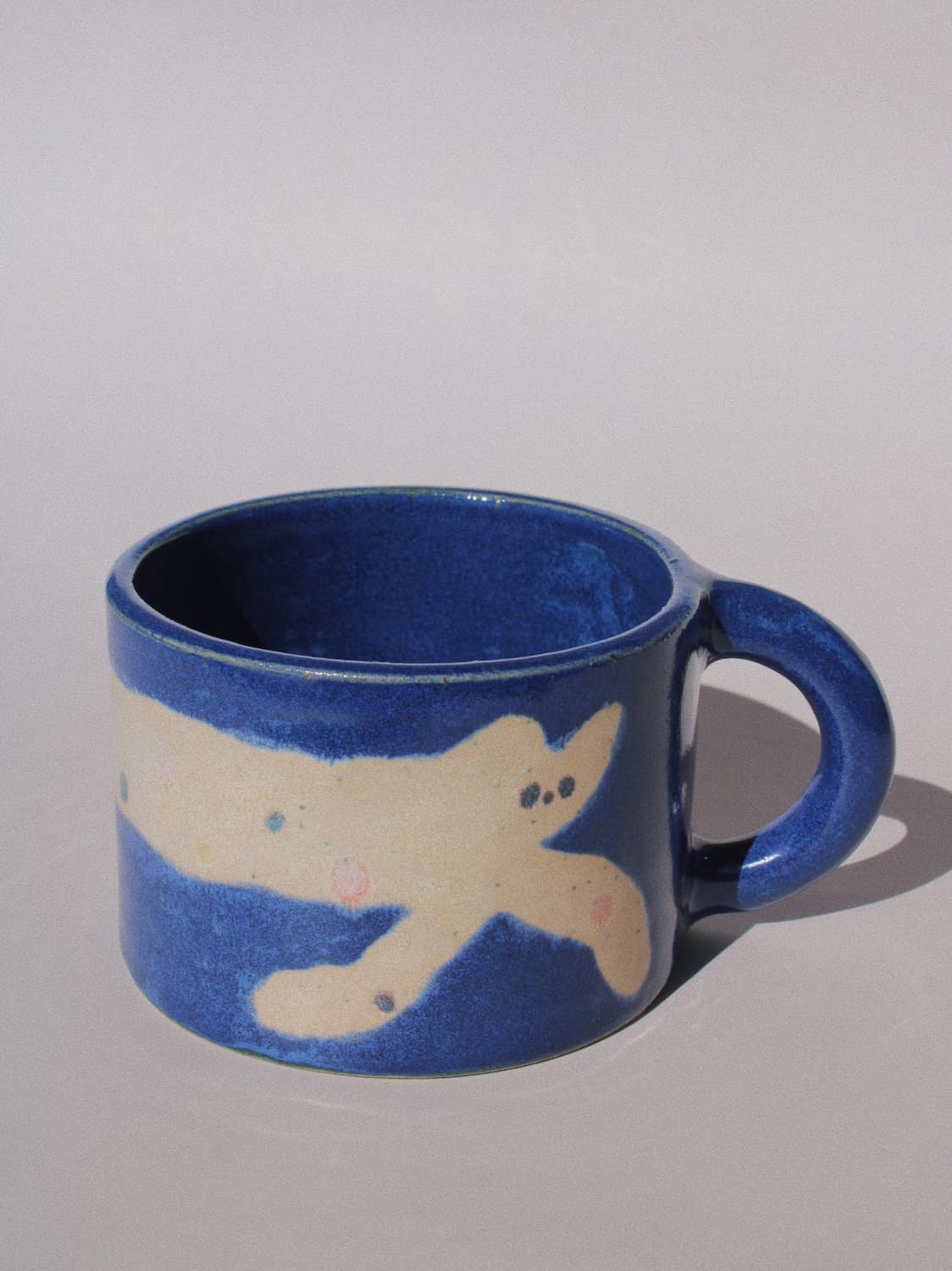 Moonmilk Cat Ceramic Mug by Marta Shurpakova – handmade blue ceramic mug with a playful cat design on a pink background