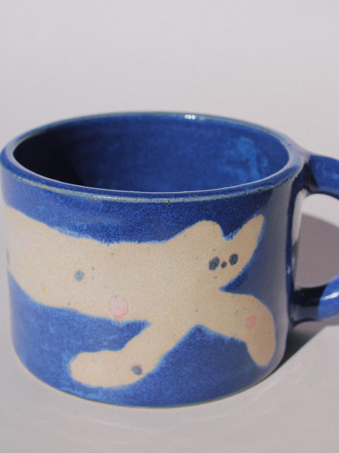 Moonmilk Cat Ceramic Mug by Marta Shurpakova – handmade blue ceramic mug with a playful cat design on a pink background