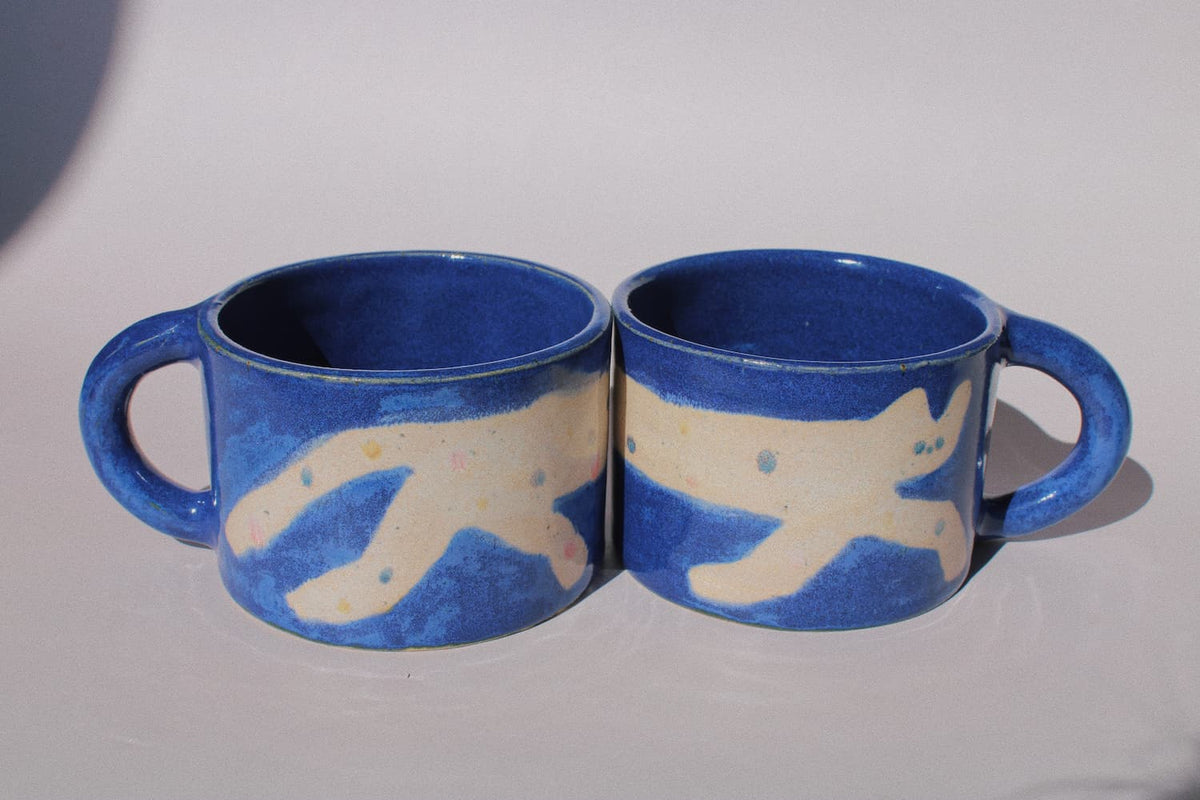 Moonmilk Cat Ceramic Mug by Marta Shurpakova – handmade blue ceramic mug with a playful cat design on a pink background