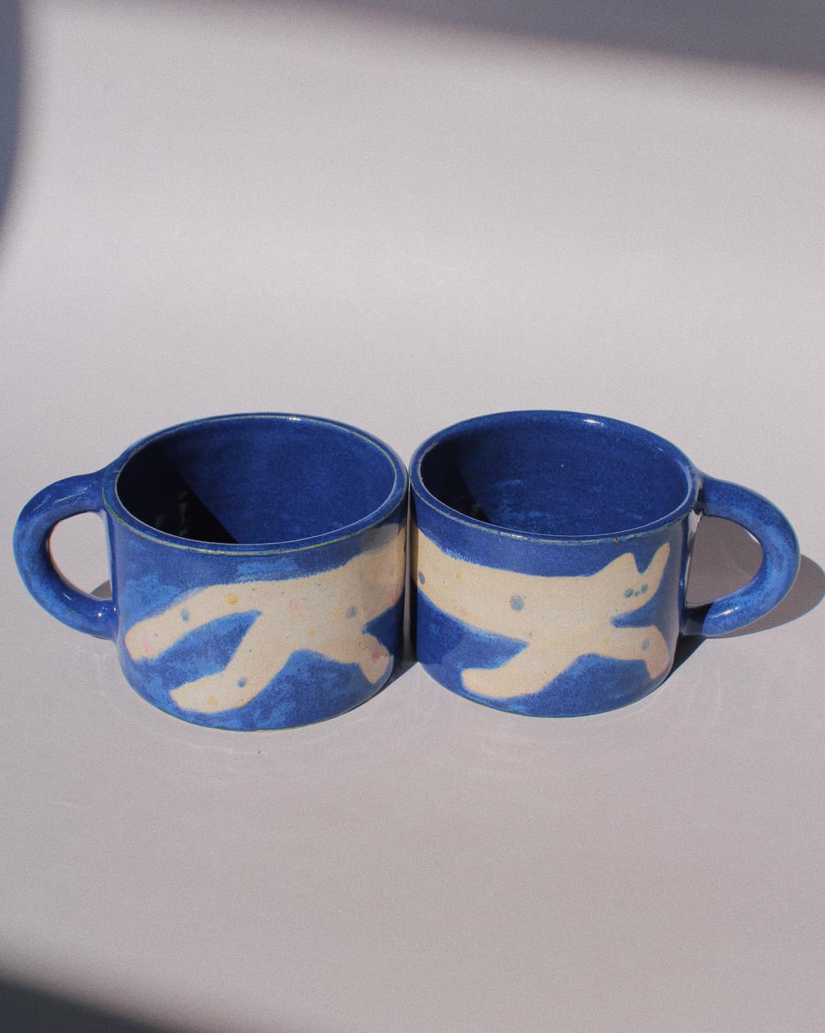 Moonmilk Cat Ceramic Mug by Marta Shurpakova – handmade blue ceramic mug with a playful cat design on a pink background