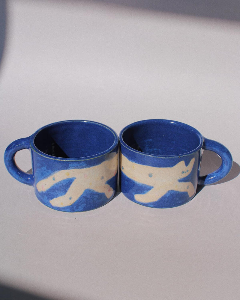 Moonmilk Cat Ceramic Mug by Marta Shurpakova – handmade blue ceramic mug with a playful cat design on a pink background