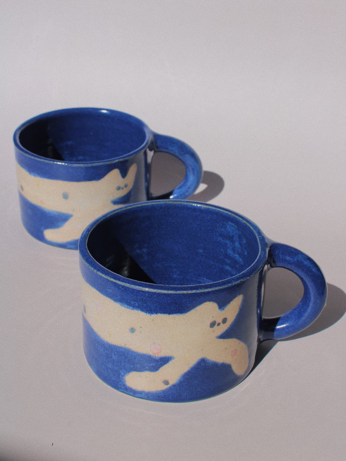 Moonmilk Cat Ceramic Mug by Marta Shurpakova – handmade blue ceramic mug with a playful cat design on a pink background