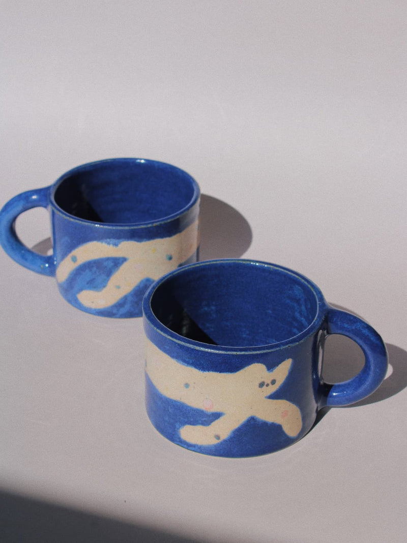 Moonmilk Cat Ceramic Mug by Marta Shurpakova – handmade blue ceramic mug with a playful cat design on a pink background