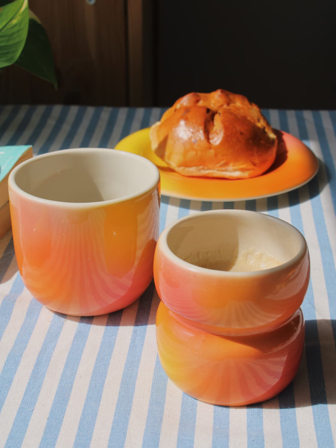 Sunset Gradient Ceramic Cup by Agata Puławska – colourful handmade ceramic cups styled with coffee and a pastry on a blue striped tablecloth