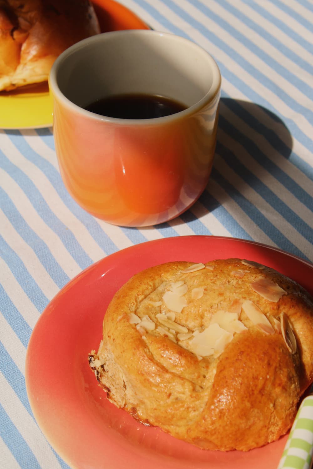 Sunset Gradient Ceramic Cup by Agata Puławska – colourful handmade ceramic cups styled with coffee and a pastry on a blue striped tablecloth