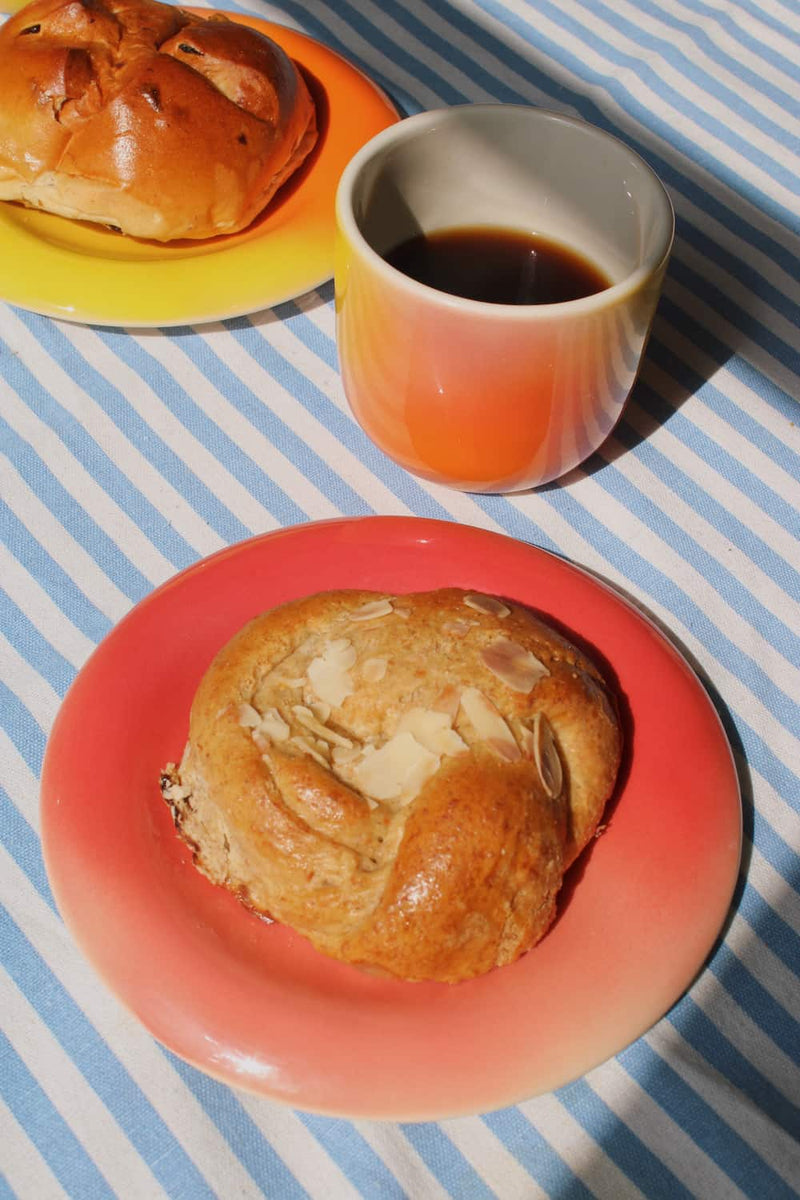 Sunset Gradient Ceramic Cup by Agata Puławska – colourful handmade ceramic cups styled with coffee and a pastry on a blue striped tablecloth